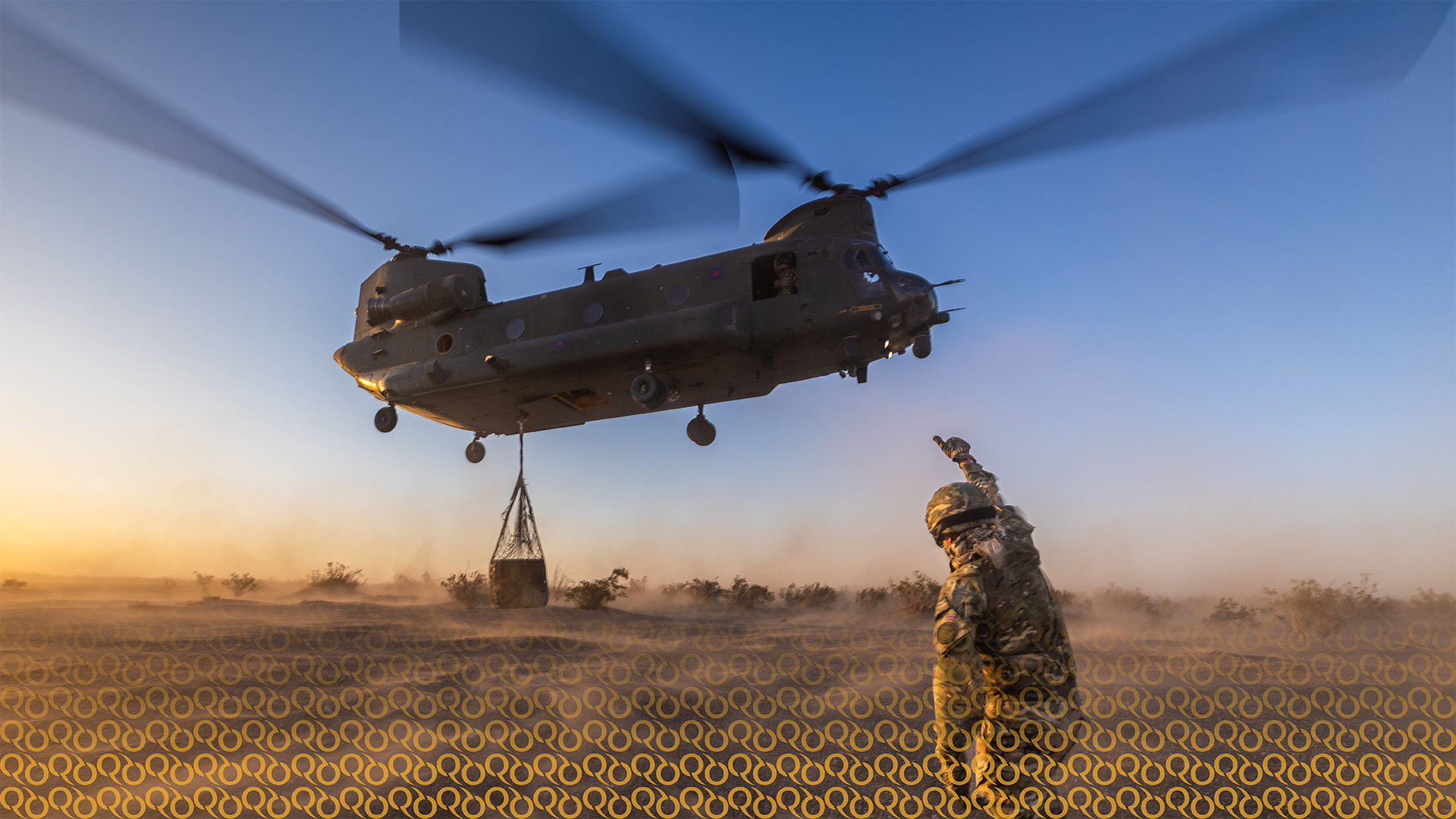 Military chinook helicopter with cargo hanging below, being guided towards the ground by army personnel